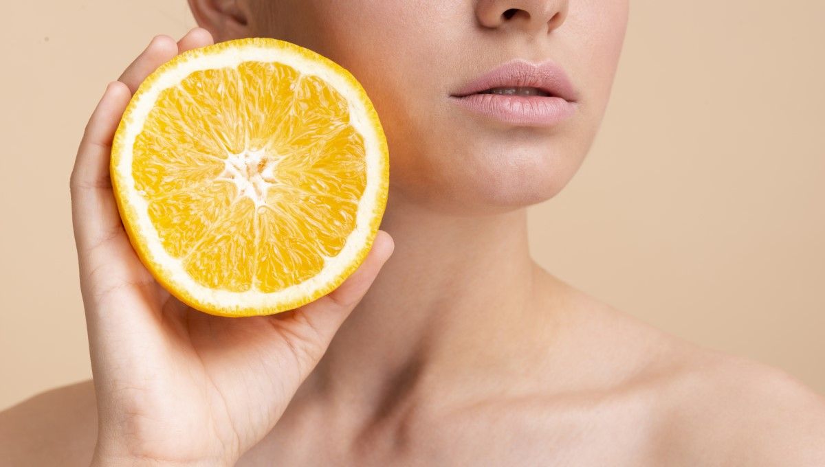 Mujer sosteniendo una naranja, alimento rico en vitamina C, en su mano (Foto. Freepik)